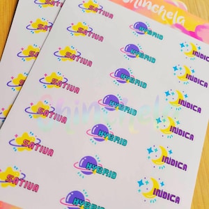 Puede incluir: Hojas de pegatinas con diseños coloridos. Las pegatinas presentan las palabras "SATIVA", "HYBRID" e "INDICA" en varias fuentes y colores, junto con gráficos de planetas, lunas y estrellas. La marca "Chinchela" también es visible.