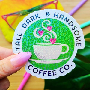 Könnte beinhalten: Ein runder Aufkleber in Grün und Weiß mit Glitzer. Der Aufkleber zeigt eine Kaffeetasse mit Dampf und Herzen und den Text "Tall Dark & Handsome Coffee Co."