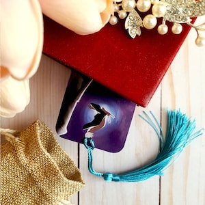 May include: A purple bookmark with a blue and white design of a bird in flight. The bookmark has a turquoise tassel.