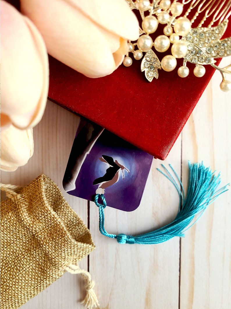 May include: A purple bookmark with a blue and white design of a bird in flight. The bookmark has a turquoise tassel.