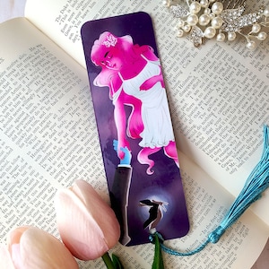 May include: A bookmark featuring a pink and white illustration of a woman with a crown of flowers and a man in a suit. The woman is holding the man's hand and they are standing on a purple background with a silhouette of a woman in the background. The bookmark has the text "The Stranger" at the top.