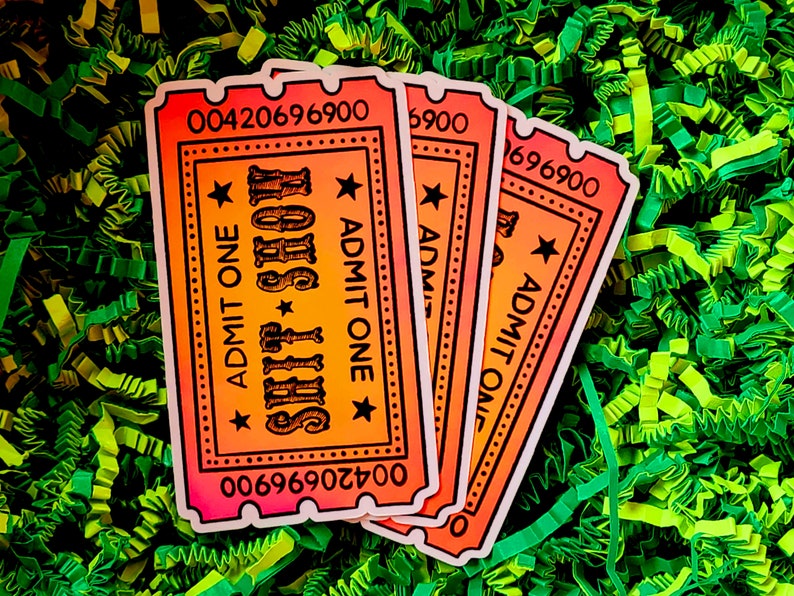 May include: Three orange, pink, and yellow ticket-shaped stickers with the text "SHIT SHOW" and "ADMIT ONE" printed on them. The stickers are on a green and yellow shredded paper background.