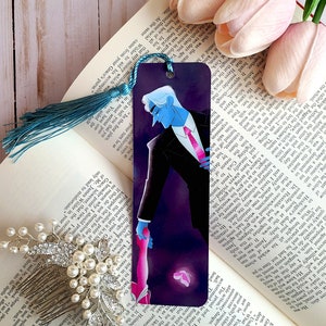 May include: A bookmark featuring a blue-skinned man in a black suit and red tie, holding the hand of a pink-skinned woman with a butterfly behind them. The bookmark has a teal tassel.