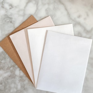 May include: Four sheets of paper in different shades of brown, pink, and white. The sheets are arranged in a fan shape on a marble surface.