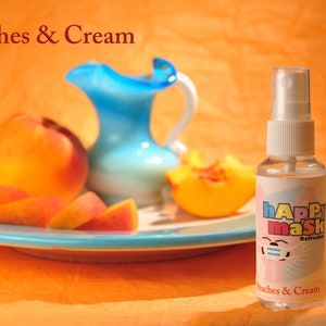 May include: A clear glass bottle with a white spray top and a colorful label that says "happy mask" and "Peaches & Cream". The bottle is sitting on a blue plate with sliced peaches.