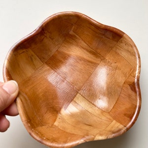 May include: A woven wooden bowl with a wavy edge. The bowl is made of light brown wood and has a square pattern.