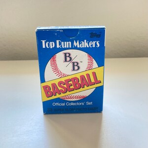 May include: A blue and yellow box of Topps baseball cards featuring a baseball with the text "Top Run Makers" and "B/B Baseball" with the text "Official Collectors' Set 33 Super Gloss Photo Cards".