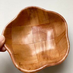 May include: A woven wooden bowl with a wavy, scalloped edge. The bowl is made of light brown wood and has a natural finish.