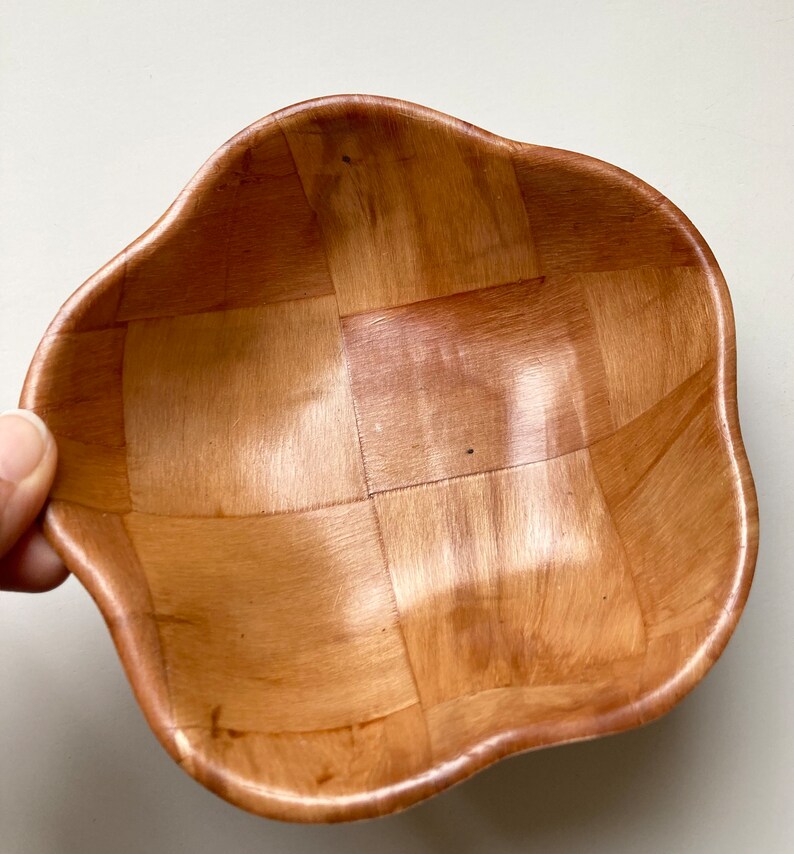May include: A woven wooden bowl with a wavy, scalloped edge. The bowl is made of light brown wood and has a natural finish.