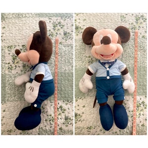 May include: A plush Mickey Mouse toy wearing a blue shirt with a white collar and a bow tie. He is wearing blue pants and brown shoes. The toy is approximately 18 inches tall.
