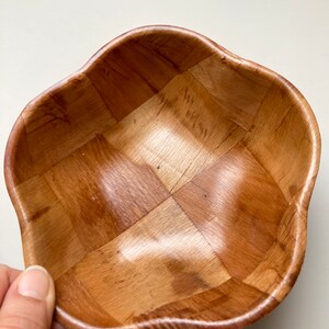 May include: A woven wooden bowl with a light brown color and a wavy rim. The bowl is made of thin strips of wood that are woven together to create a checkered pattern.