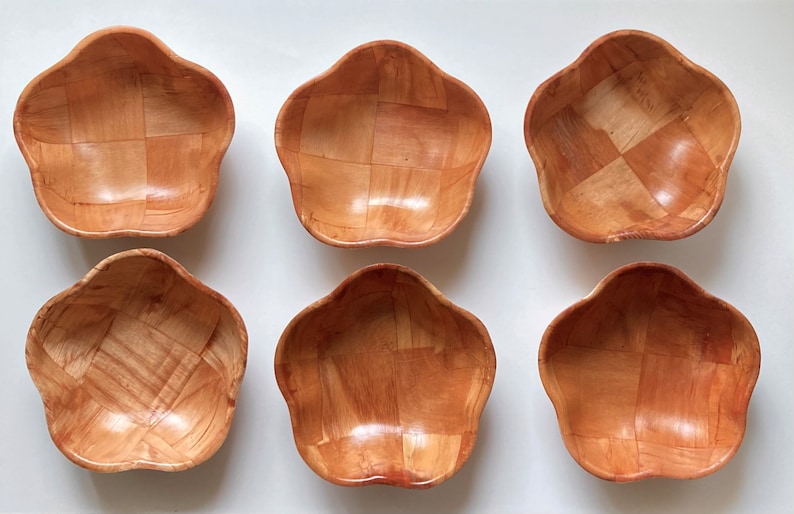 May include: Six small, wooden bowls in a light brown color. The bowls are shaped like a flower with five petals and have a woven pattern.