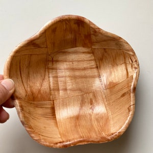 May include: A woven wooden bowl with a light brown color and a wavy, irregular shape.