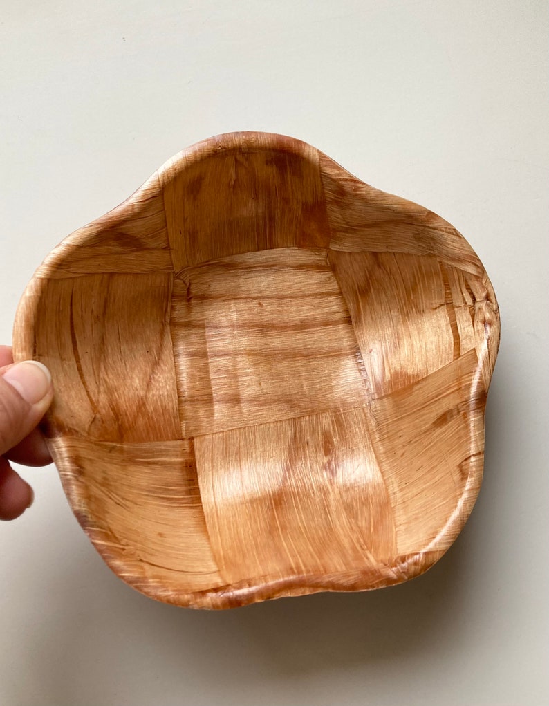May include: A woven wooden bowl with a light brown color and a wavy, irregular shape.