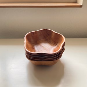 May include: A set of four wooden bowls stacked on top of each other. The bowls are a light brown color and have a wavy, flower-like shape.
