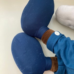 May include: A plush toy with blue fabric and brown fabric accents. The toy has two large, round, blue feet.