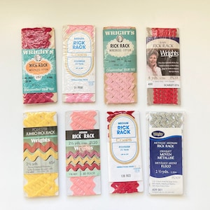 May include: Assortment of eight packages of Wright's Rick Rack trim in various colors and sizes. The packages feature different types of rick rack, including baby rick rack, medium rick rack, jumbo rick rack, and metallic rick rack. The packages are labeled with the type of rick rack, the color, the size, and the price.