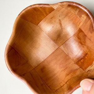 May include: A wooden bowl with a woven pattern. The bowl is light brown and has a rounded, scalloped edge.