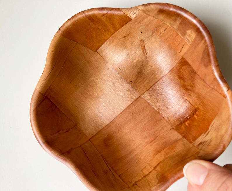 May include: A wooden bowl with a woven pattern. The bowl is light brown and has a rounded, scalloped edge.