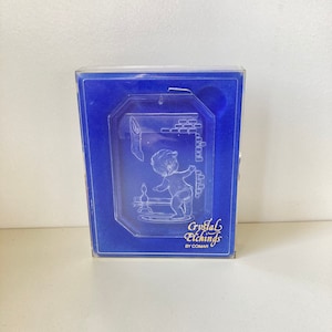 May include: A clear glass etched ornament of a baby in a bathtub with a duck. The ornament is in a blue velvet box with the words "Crystal Etchings by Comar" on the bottom.