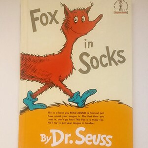 May include: A book cover featuring a red fox wearing blue socks. The title is "Fox in Socks" by Dr. Seuss. The book is part of the Beginner Books series.