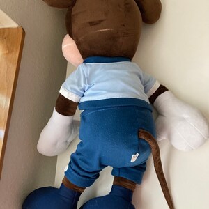 May include: A large brown and blue plush Mickey Mouse toy. The toy is wearing a blue shirt and blue pants. The toy has a long brown tail.