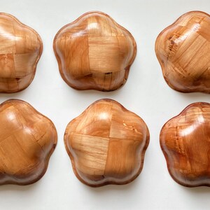 May include: Six wooden bowls with a woven pattern. The bowls are light brown and have a rounded, flower-like shape.