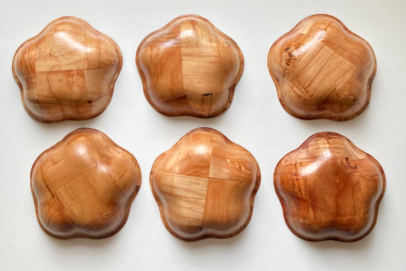 May include: Six wooden bowls with a woven pattern. The bowls are light brown and have a rounded, flower-like shape.