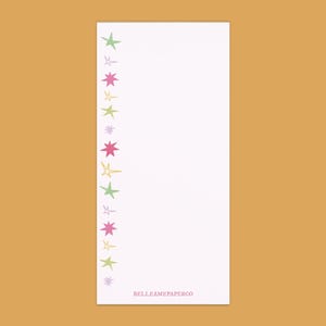 May include: A white notepad with a vertical row of colorful star illustrations in green, pink, and yellow. The notepad has the text "BELLSAMEPAPERCO" at the bottom.