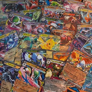 May include: A collection of assorted trading cards featuring various colorful illustrated creatures, including Pikachu, Ho-Oh, and Yveltal. Each card displays unique character artwork, power statistics, and text labels in a dense, overlapping arrangement.
