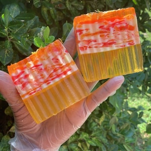 Puede incluir: Dos barras de jab&oacute;n hecho a mano con un dise&ntilde;o de remolino en tonos naranja, amarillo y blanco. El jab&oacute;n est&aacute; en capas con una base naranja transl&uacute;cida y un dise&ntilde;o de remolino blanco.