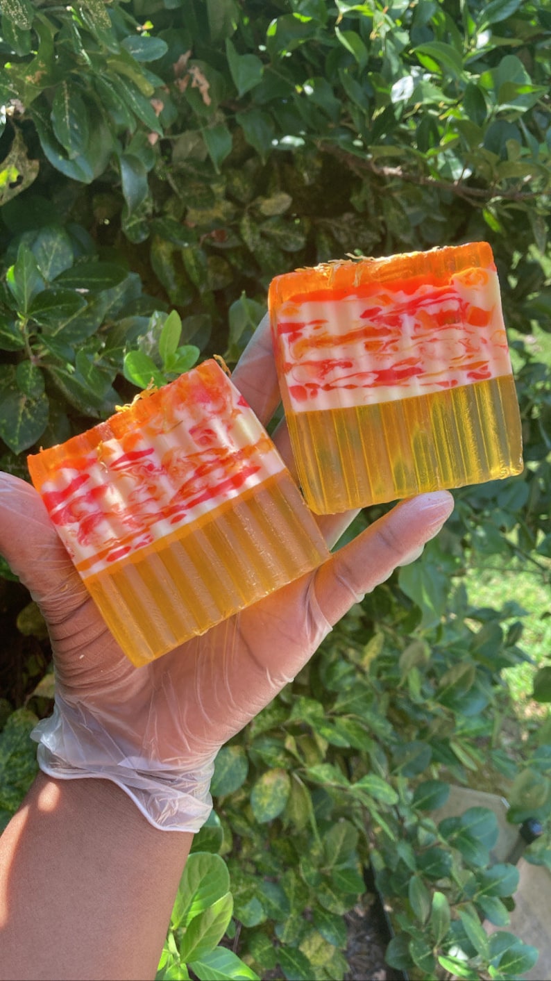 Puede incluir: Dos barras de jab&oacute;n hecho a mano con un dise&ntilde;o de remolino en tonos naranja, amarillo y blanco. El jab&oacute;n est&aacute; en capas con una base naranja transl&uacute;cida y un dise&ntilde;o de remolino blanco.