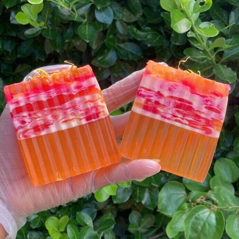 Puede incluir: Dos barras de jab&oacute;n hechas a mano con un dise&ntilde;o en capas. El jab&oacute;n es naranja, blanco y rosa. El jab&oacute;n est&aacute; hecho con ingredientes naturales.