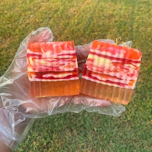 Puede incluir: Dos barras rectangulares de jab&oacute;n con un patr&oacute;n a rayas en tonos rojos, naranjas, blancos y amarillos. Las barras de jab&oacute;n est&aacute;n sobre un guante de pl&aacute;stico.