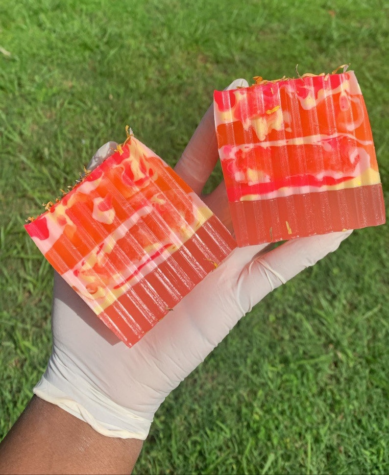 Puede incluir: Dos barras de jab&oacute;n hechas a mano con un dise&ntilde;o en capas de rosa, naranja y amarillo. Las barras de jab&oacute;n tienen un patr&oacute;n de remolino y est&aacute;n decoradas con flores secas.