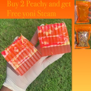 Puede incluir: Dos barras de jab&oacute;n de color melocot&oacute;n con un dise&ntilde;o de remolino blanco. Las barras de jab&oacute;n est&aacute;n en una mano que lleva un guante blanco. El texto "Buy 2 Peachy and get Free Yoni Steam" est&aacute; en la parte superior de la imagen.
