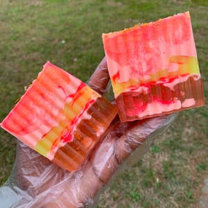 Puede incluir: Dos barras de jab&oacute;n hechas a mano con un dise&ntilde;o de remolino rosa, amarillo y naranja. El jab&oacute;n es transl&uacute;cido y tiene un aspecto en capas.