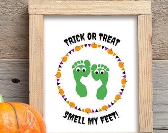 May include: A framed print with a white background and black text that reads "Trick or Treat Smell My Feet!"  The text is surrounded by a circle of green footprints with googly eyes and orange and purple pumpkins.