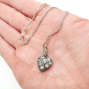 May include: A silver chain necklace with a heart-shaped pendant. The pendant is set with clear rhinestones.
