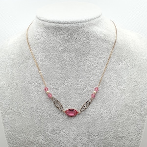 May include: A gold chain necklace with a pink oval-shaped gemstone pendant and pink and white crystal beads.