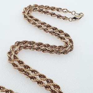 May include: A gold-toned rope chain necklace with a double strand design. The chain is made of a twisted rope pattern and has a lobster claw clasp.