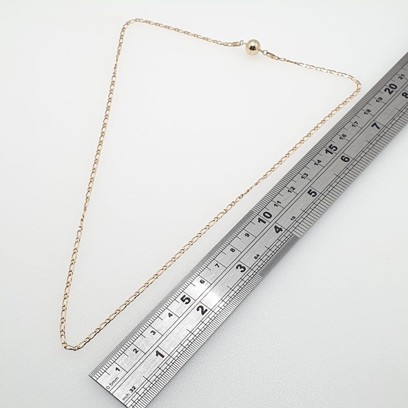 May include: A gold chain necklace with a small ball clasp. The chain is measured against a ruler, showing it is 18 inches long.