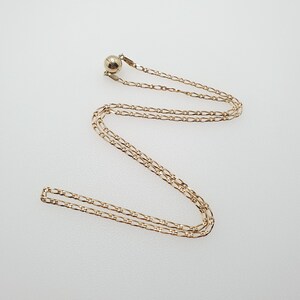 May include: A gold chain necklace with a small round pendant. The chain is a delicate, fine link style.