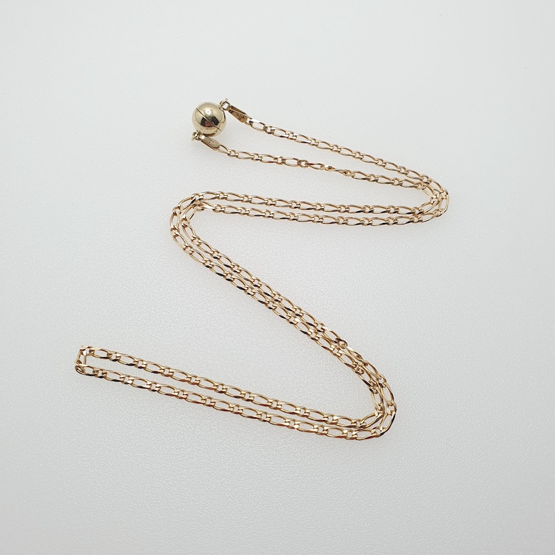 May include: A gold chain necklace with a small round pendant. The chain is a delicate, fine link style.