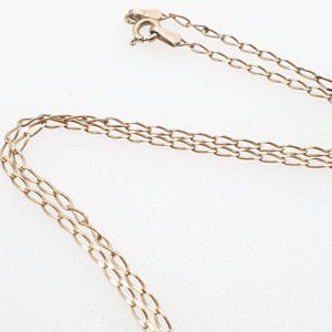 May include: A delicate gold-colored necklace with a chain link design. The necklace is shown against a white background, with the clasp visible at the top. The chain is made of small, oval-shaped links.