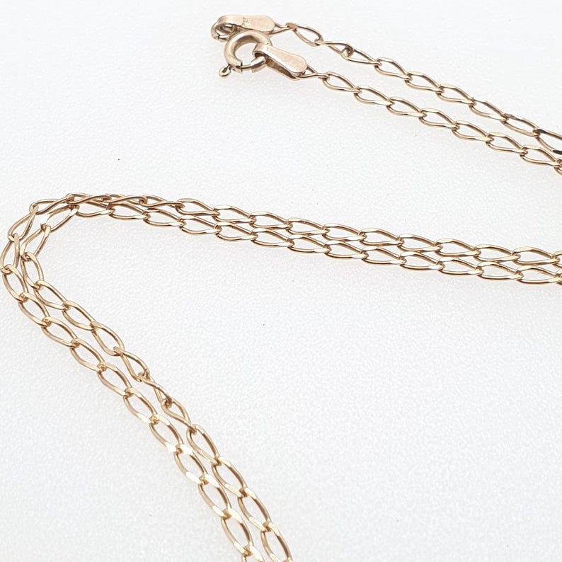 May include: A delicate gold-colored necklace with a chain link design. The necklace is shown against a white background, with the clasp visible at the top. The chain is made of small, oval-shaped links.