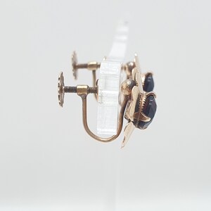 May include: A pair of gold-tone earrings with black gemstone accents. The earrings have a flower-shaped design and a screw-back fastening.