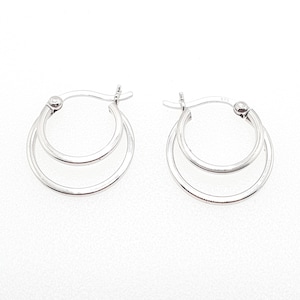 May include: A pair of silver hoop earrings. Each earring has a double-hoop design, with one hoop inside the other. The earrings have a polished, reflective surface and a simple, elegant style. They are displayed on a white background.