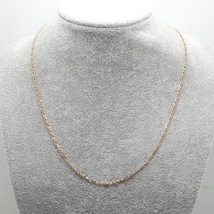 May include: A gold chain necklace on a gray background.