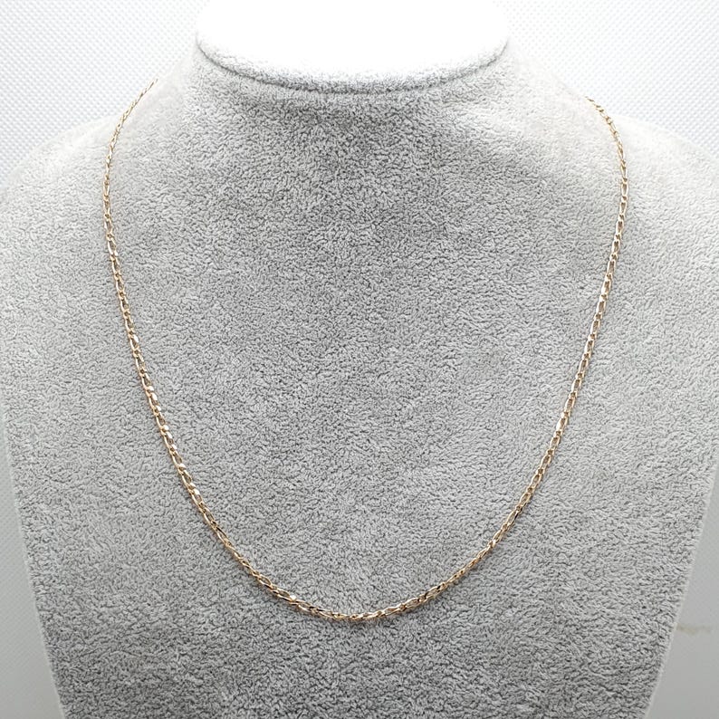 May include: A gold chain necklace on a gray background.